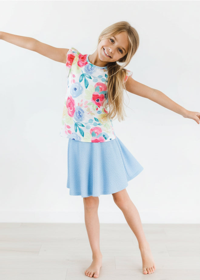 Child wearing a colorful floral top and light blue skirt on a white background