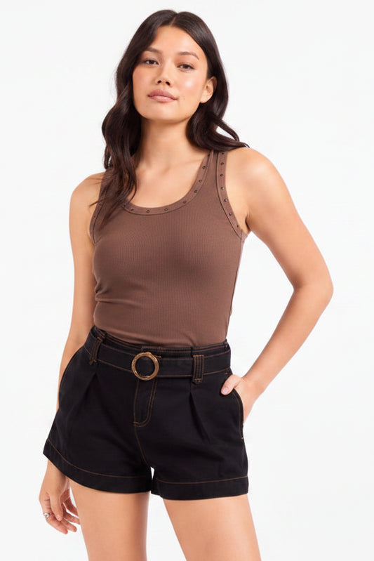 A woman modeling a brown ribbed tank top with decorative studs along the neckline, paired with black denim shorts featuring a matching belt with a round gold-tone buckle, against a plain white studio background.