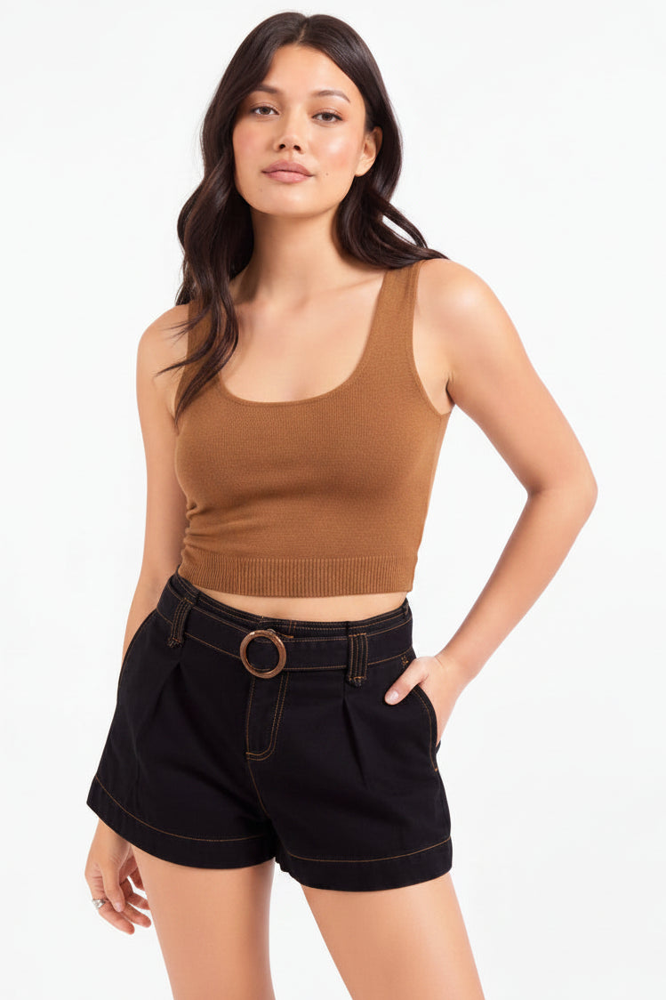 A woman modeling a brown ribbed tank top with decorative studs along the neckline, paired with black denim shorts featuring a matching belt with a round gold-tone buckle, against a plain white studio background.