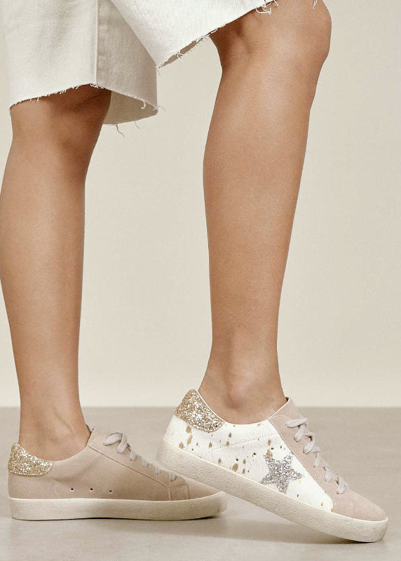 Beige sneakers with glittery accents worn by a person on a neutral background
