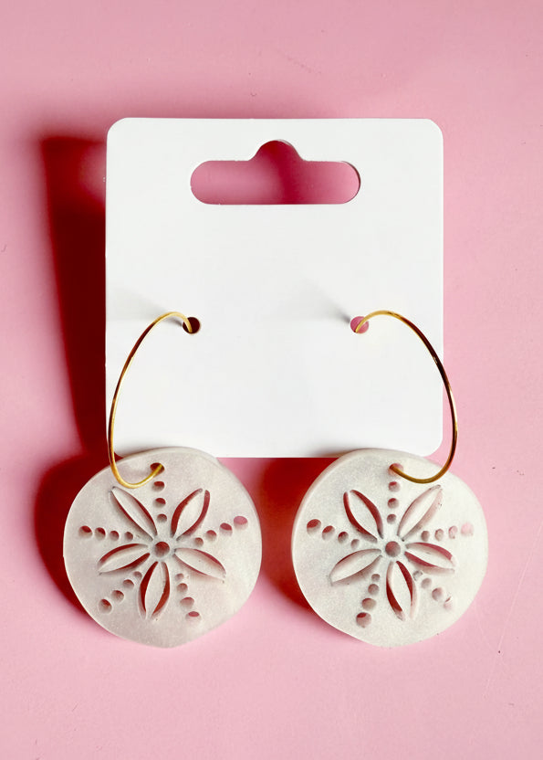 Earrings with floral design on a white card with 'SR' branding against a pink background
