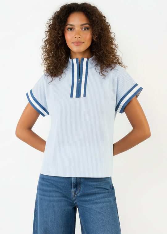 Woman wearing a light blue top with dark blue accents and white shorts on a white background