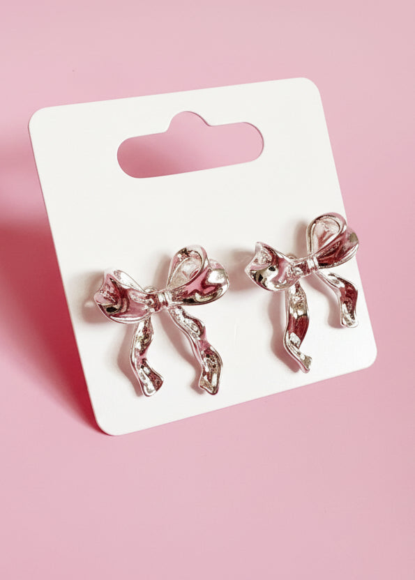 Bow-shaped earrings on a branded card against a pink background