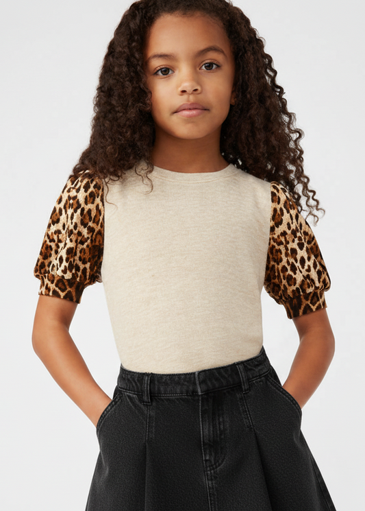 Young girl wearing a top with leopard print sleeves and black pants on a white background