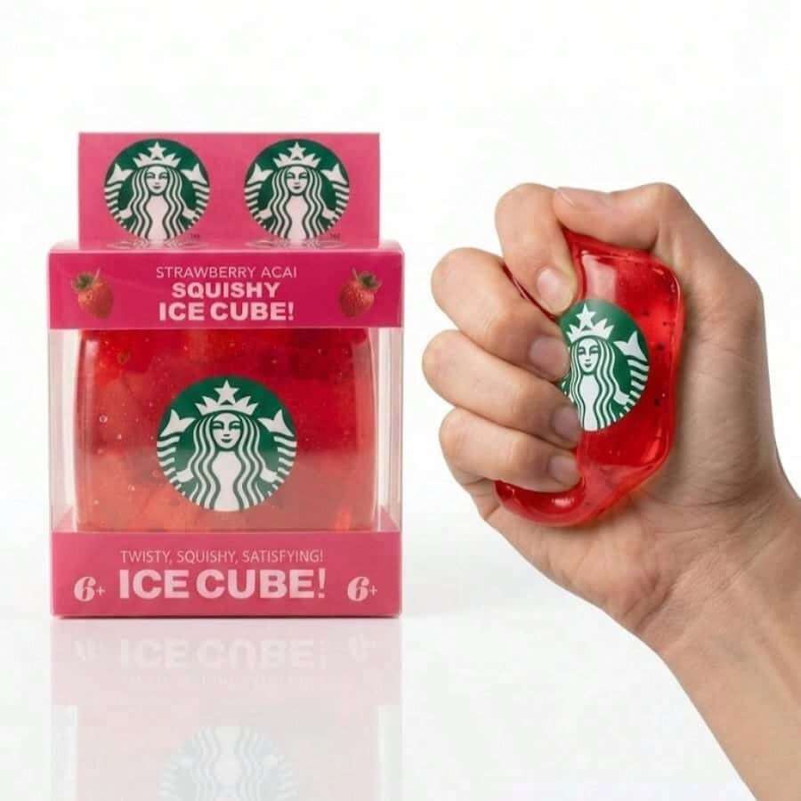 A hand holds a translucent red squishy ice cube shaped like a Starbucks logo, next to its pink retail box labeled 'Strawberry Acai Squishy Ice Cube!' on a white background.