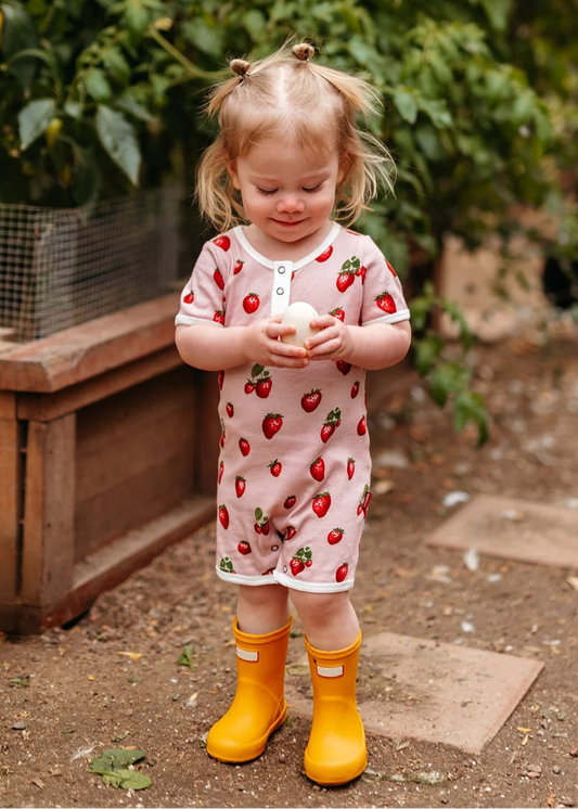 Child in strawberry dress and yellow boots standing outdoors with ducks in the background