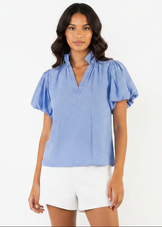 Woman wearing a blue blouse with ruffled sleeves and white shorts on a white background