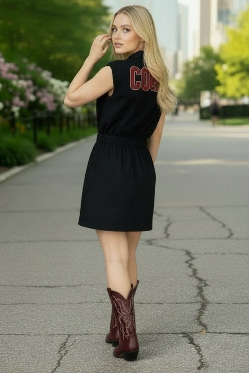 Woman in a black dress with red text and brown boots standing on a city street.