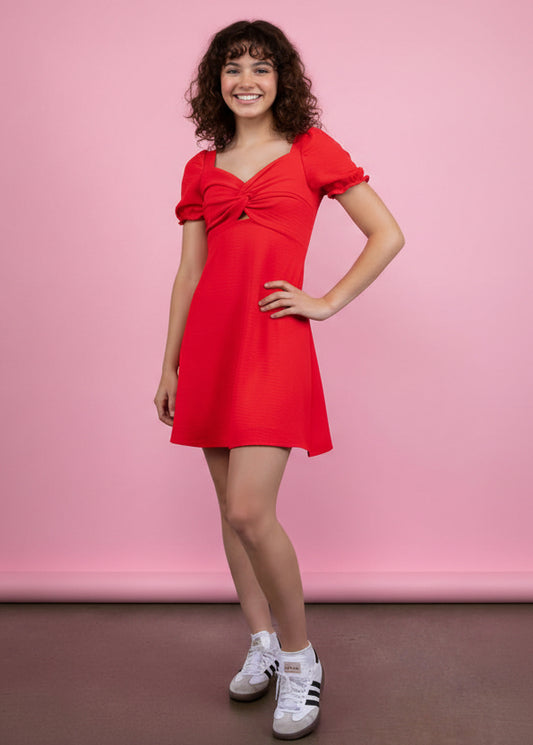 Tween girl wearing a red dress with puffed sleeves against a pink background