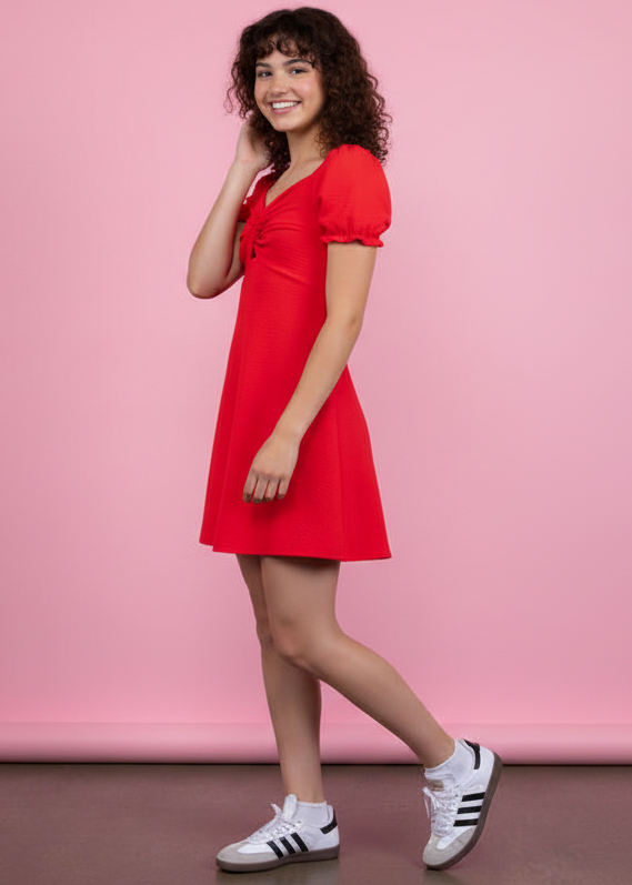 Woman wearing a red dress with white sneakers against a pink background