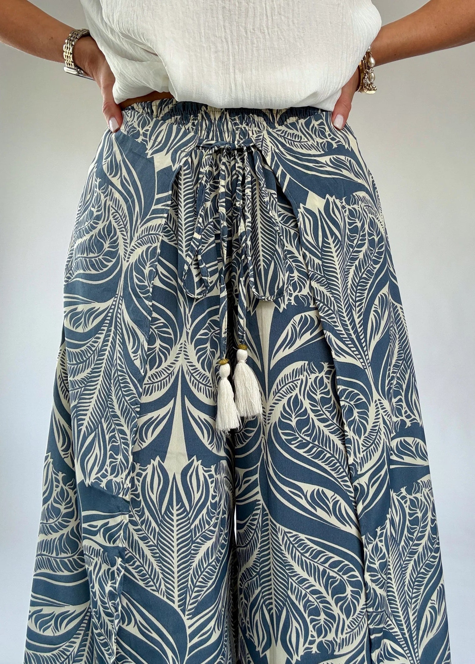 Person wearing blue and white patterned pants with tassels on a plain background