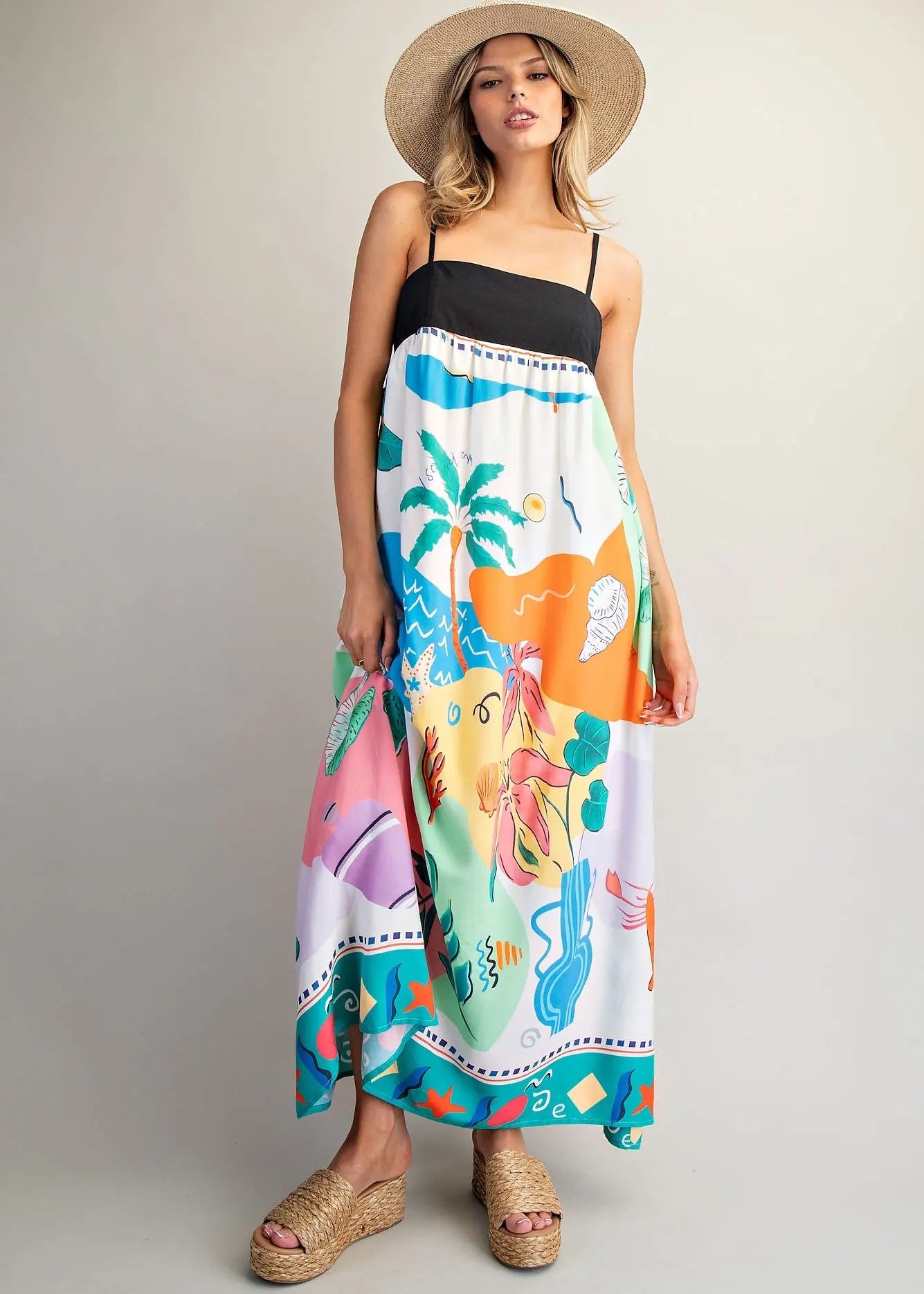 Woman wearing a colorful dress with a mermaid design and a straw hat on a plain background