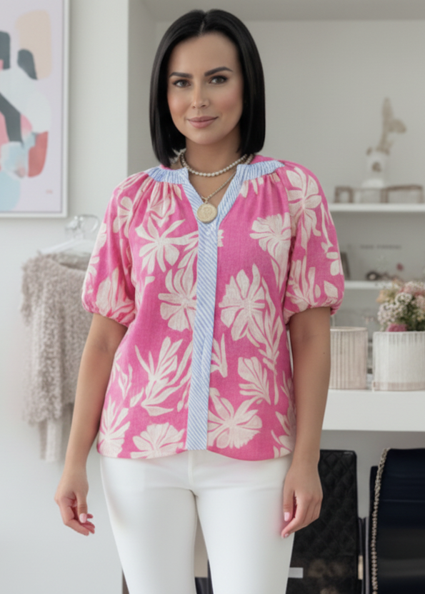Woman wearing a pink floral blouse with white pants in an indoor setting.