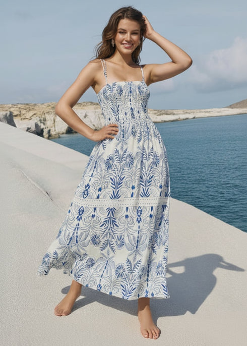 Woman in a floral dress standing by the ocean with a clear sky.