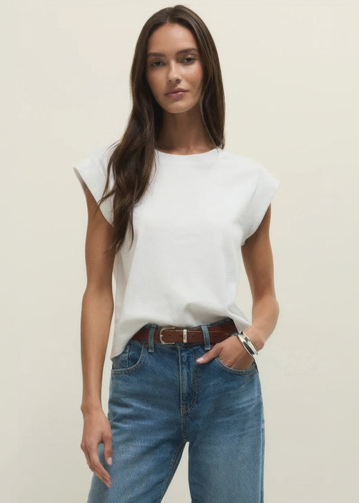 Woman wearing a white sleeveless top and blue jeans against a plain background