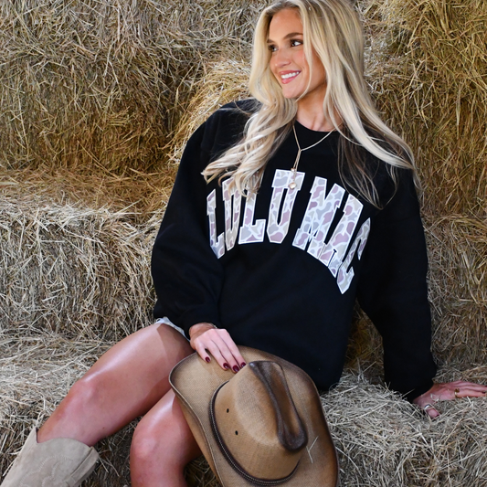 Woman wearing a black sweatshirt with 'CULU MAC' text, sitting on hay.