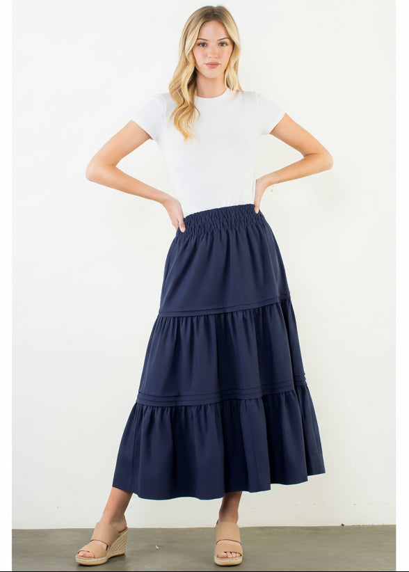 Woman wearing a white top and navy tiered skirt on a plain background