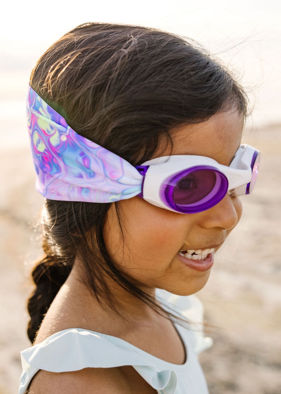Young girl wearing colorful goggles and headband in a natural setting