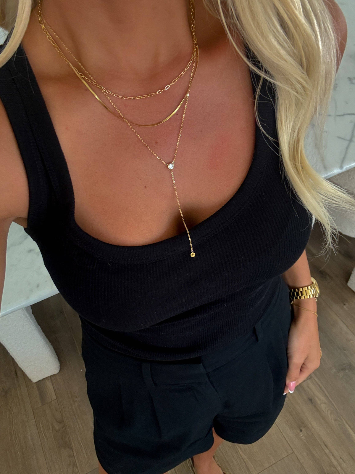 Person wearing a black top and shorts with gold necklaces and a bracelet indoors.