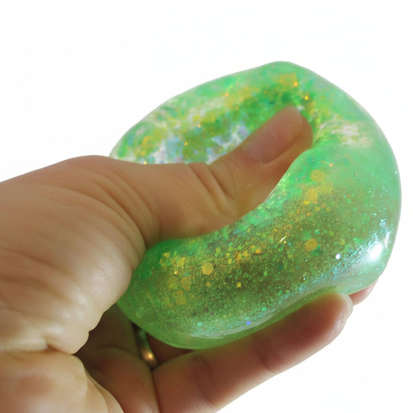 Green glittery slime held between fingers with 'Curious Minds' logo in the corner.