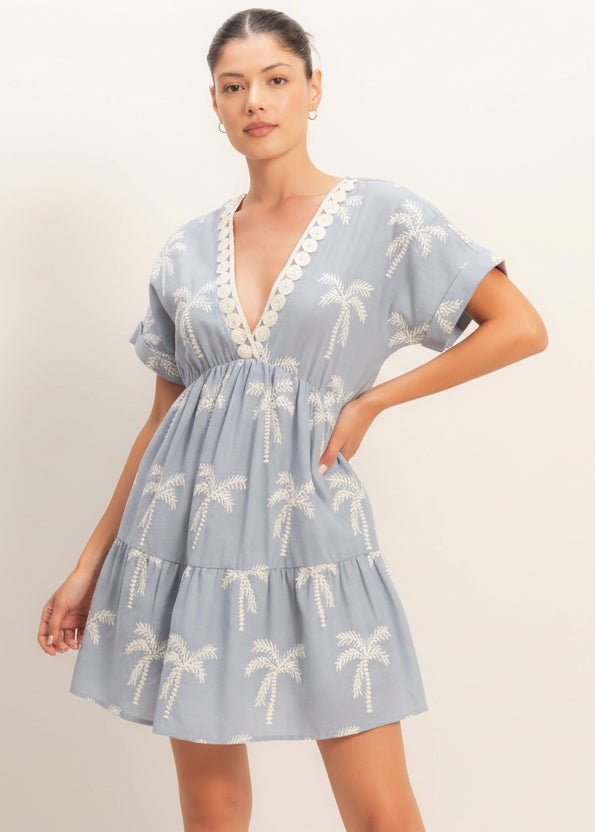 Woman wearing a light blue dress with palm tree patterns on a plain background