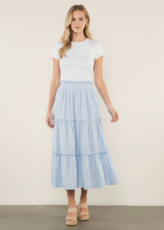 Woman wearing a white top and light blue tiered skirt on a white background