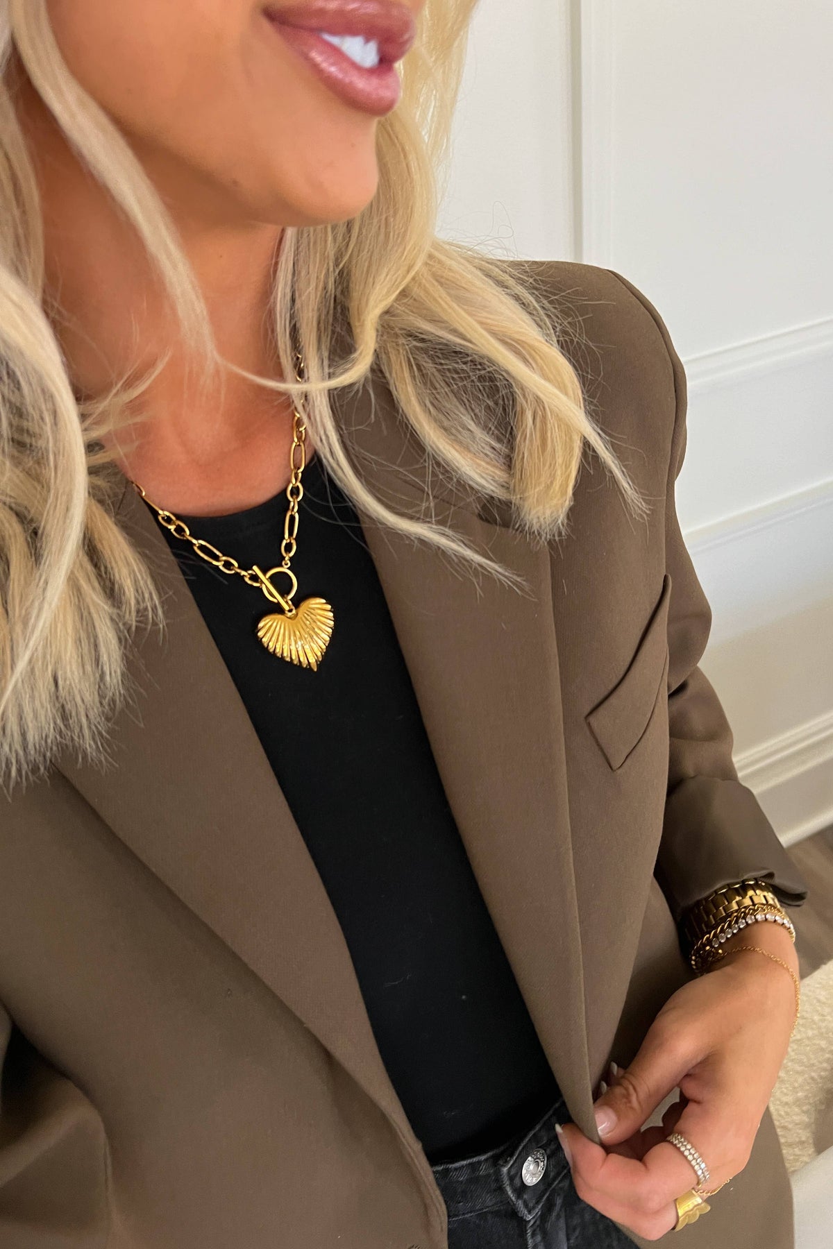 Woman wearing a brown blazer with a gold necklace and bracelet indoors.