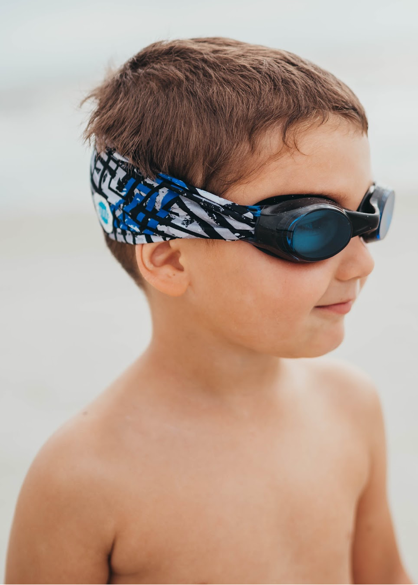 Young boy wearing swim goggles and a headband on a beach