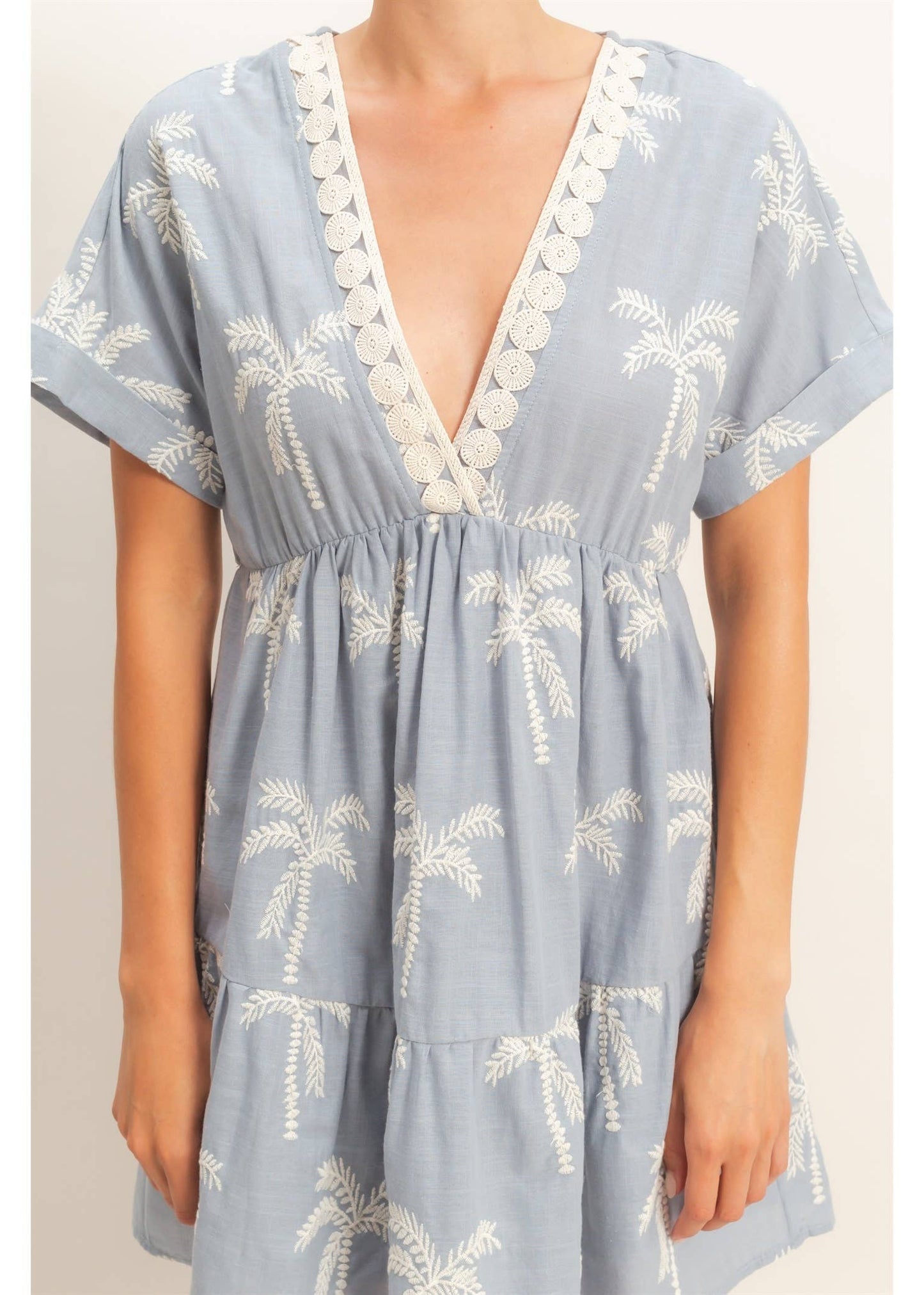 Blue dress with palm tree pattern worn by a person on a plain background