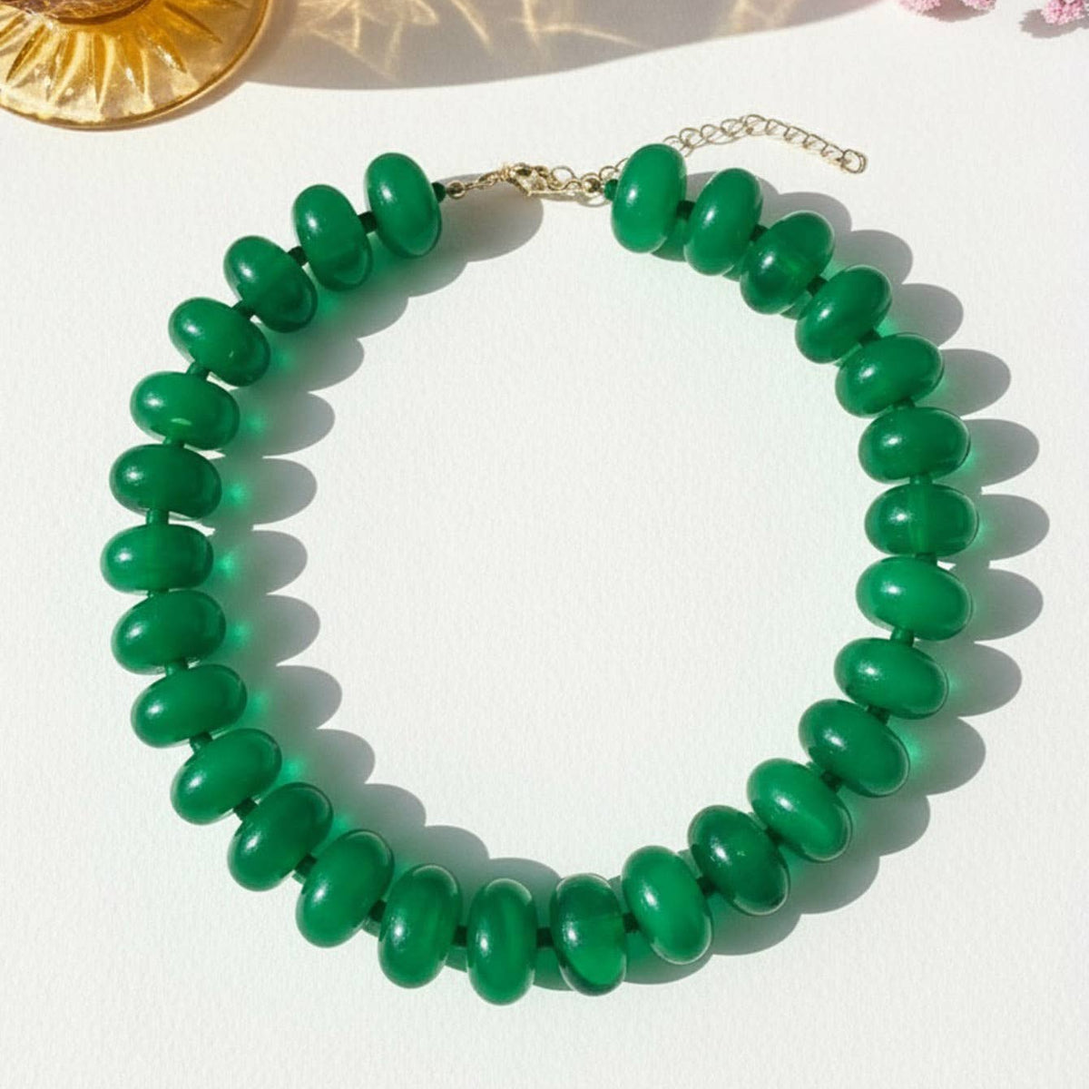Green beaded necklace on a white surface with a decorative background