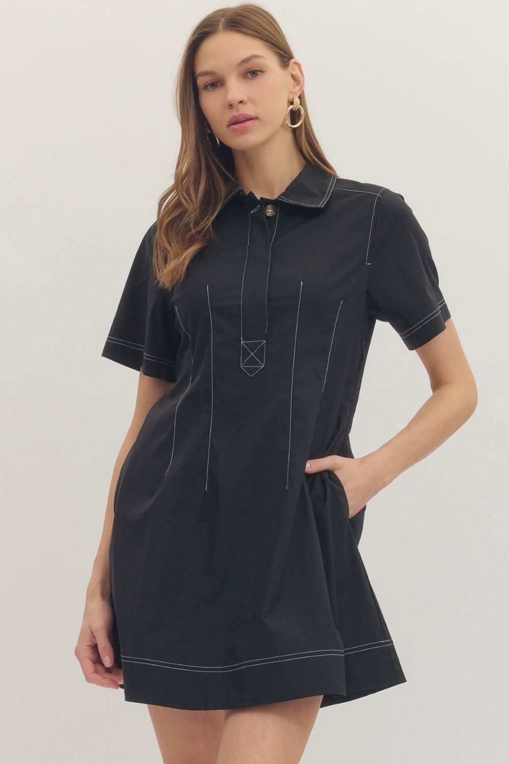 Woman wearing a black dress with white stitching on a plain background
