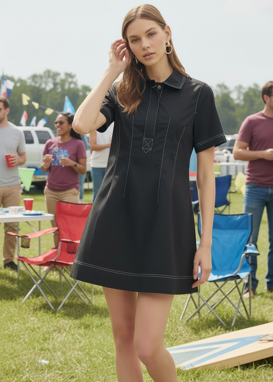 Woman in a black dress standing outdoors with people and chairs in the background
