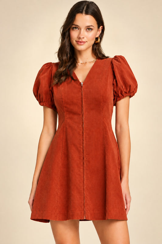 Woman wearing a rust-colored dress with puff sleeves against a gray background