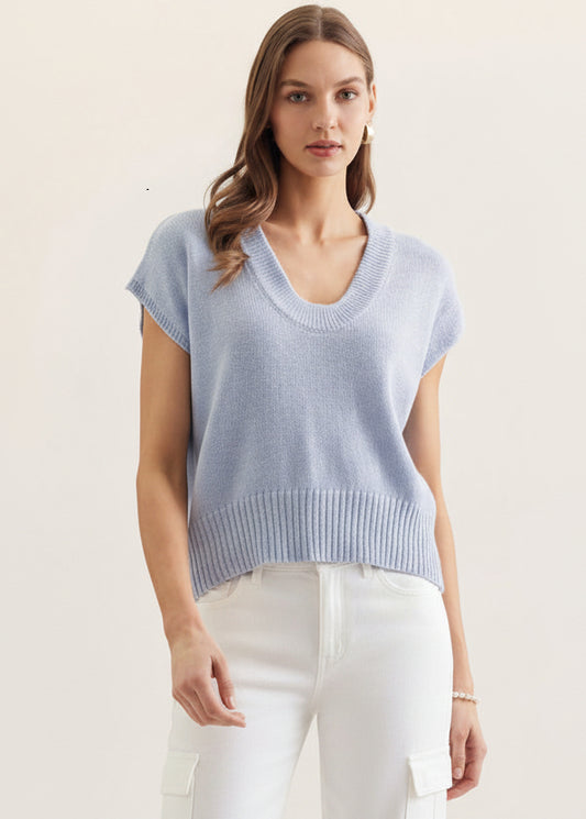 Woman wearing a light blue sleeveless sweater and white jeans on a beige background