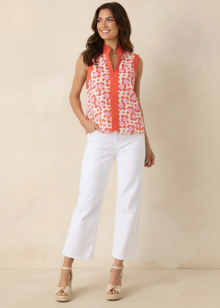 Woman wearing a colorful sleeveless top and white pants against a beige background