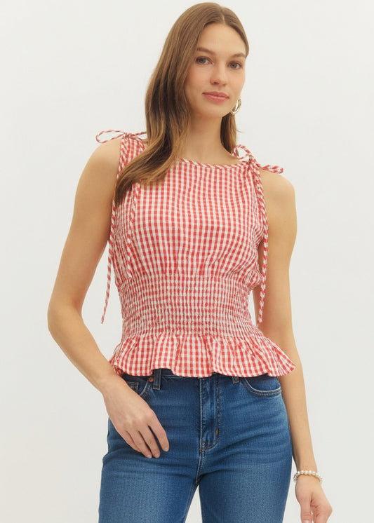 Woman wearing a red and white checkered top with ruffle details on a plain background