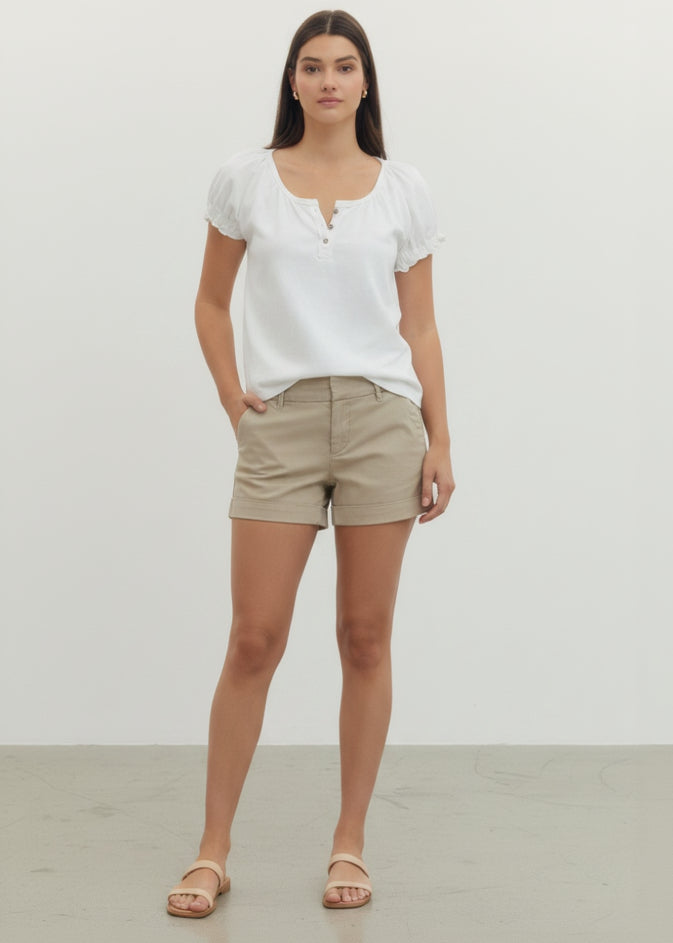 Woman wearing a white blouse and beige shorts on a plain background