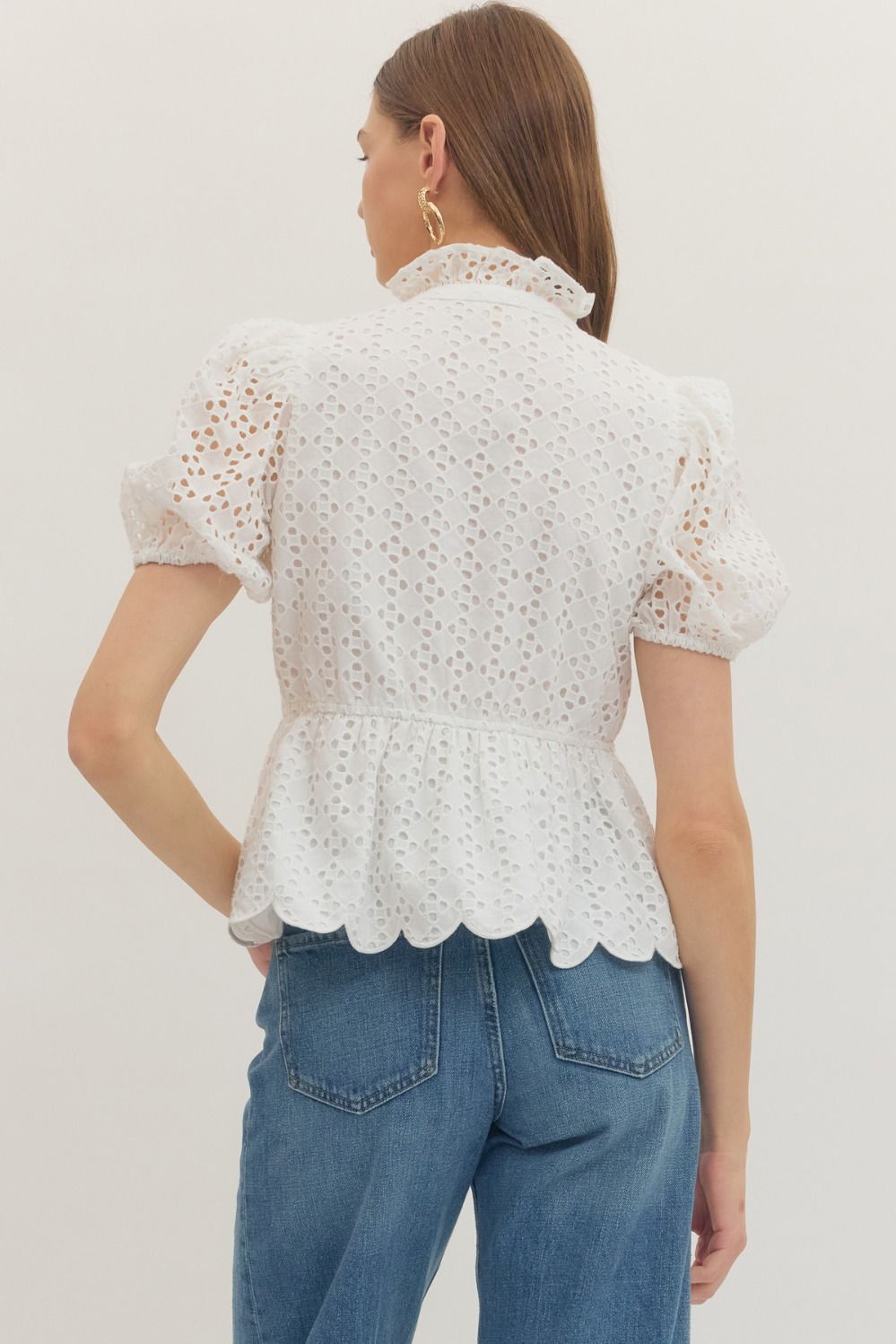 Woman wearing a white scalloped blouse and blue jeans on a plain background