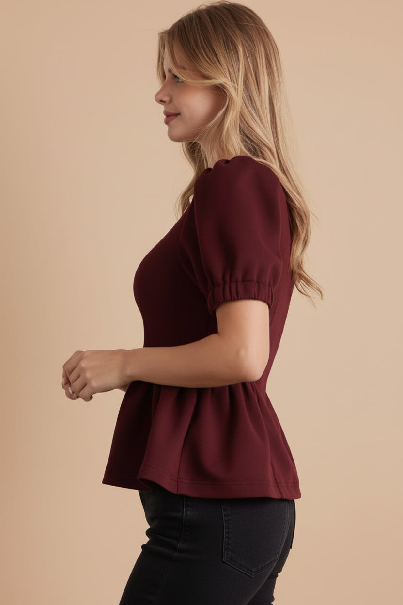 Woman wearing a burgundy top and brown polka dot skirt against a white tiled wall.