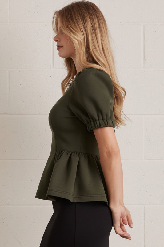 Woman wearing a green top and polka dot skirt against a white brick wall.