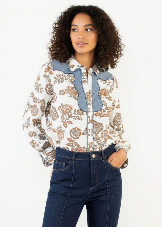 Woman wearing a patterned blouse with blue accents and dark jeans on a white background