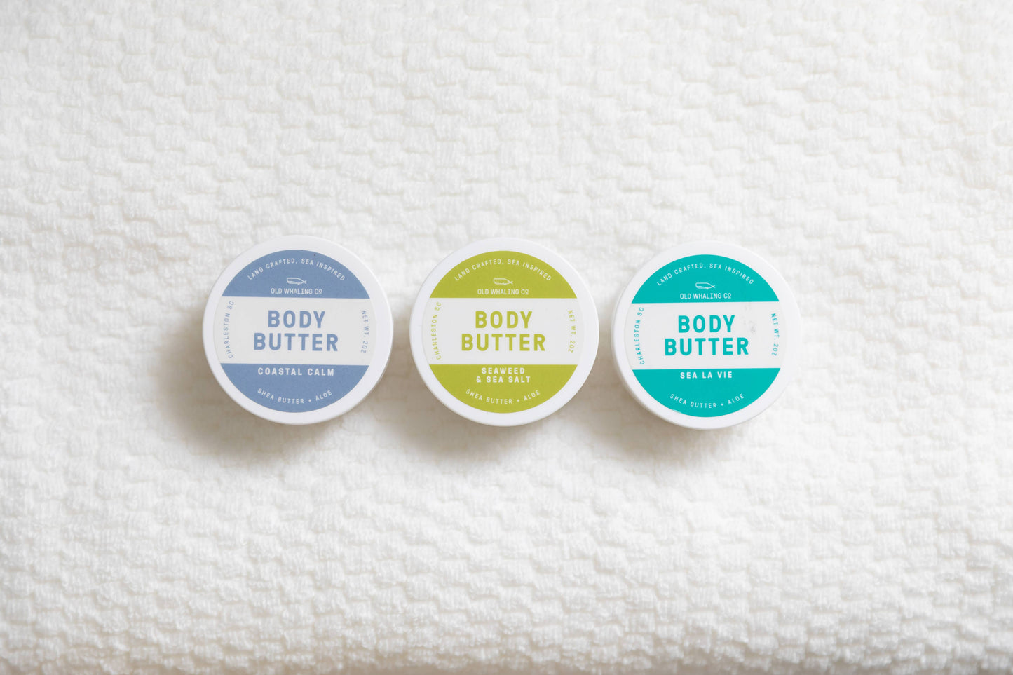 Three containers of body butter on a textured white surface