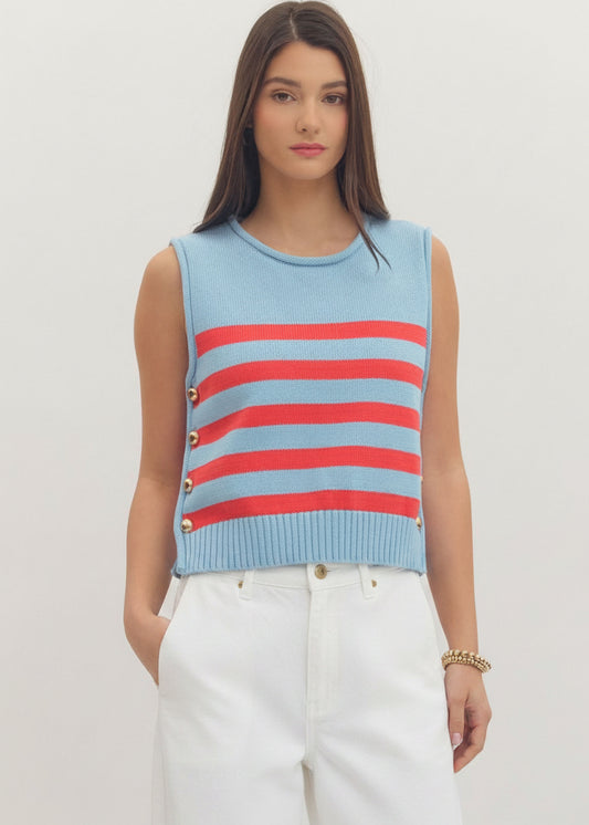 Woman wearing a light blue sleeveless sweater with red stripes on a plain background